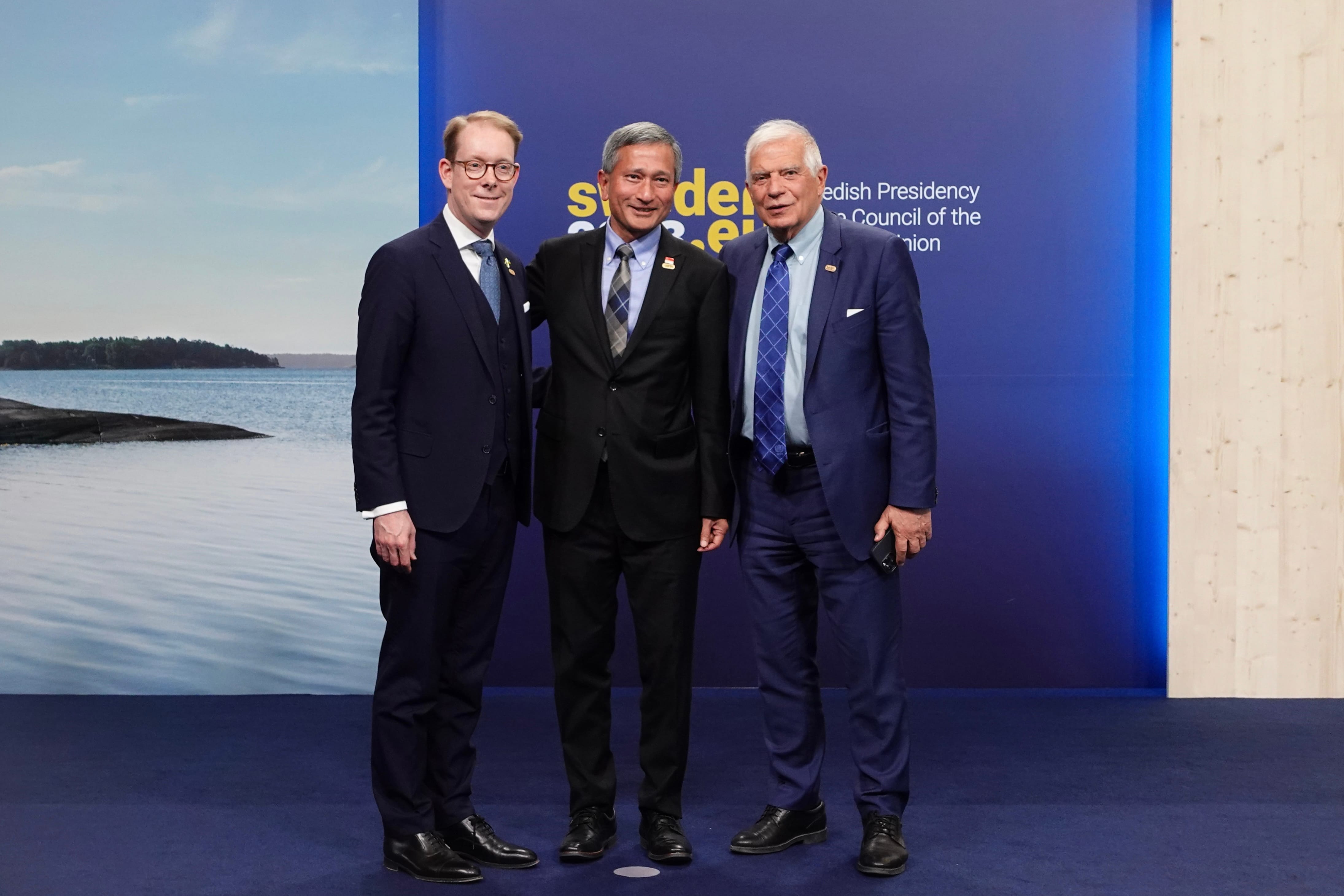 Three men in suits standing in front of a backdrop of a lake.